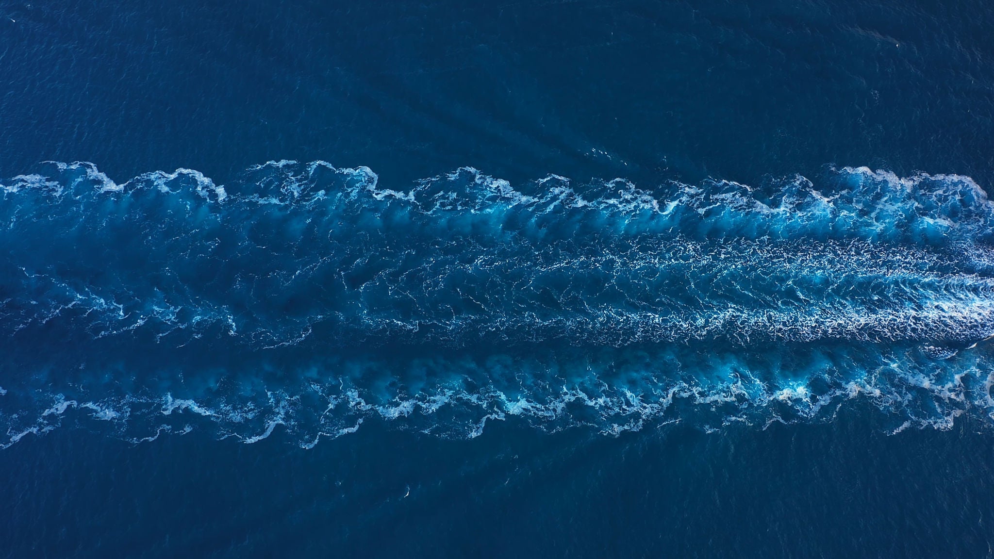 Prop wash of a tanker ship underway open sea. Aerial top down drone view of water foam trace behind a crude oil tanker