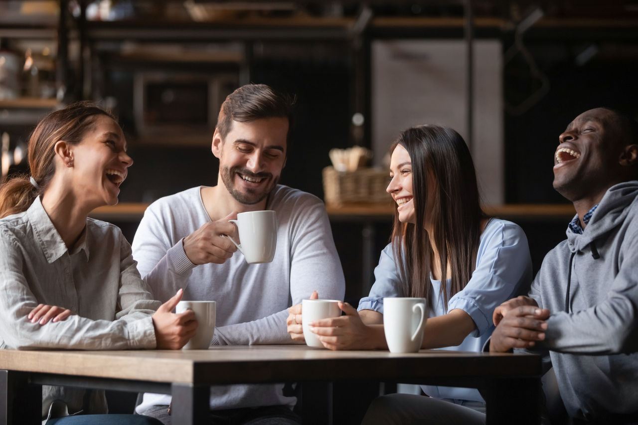 Happy multiracial friends group laugh drink tea in cafe, diverse young students talk enjoy coffee at coffeehouse meeting, multicultural people sit at table having fun together multi-ethnic friendship